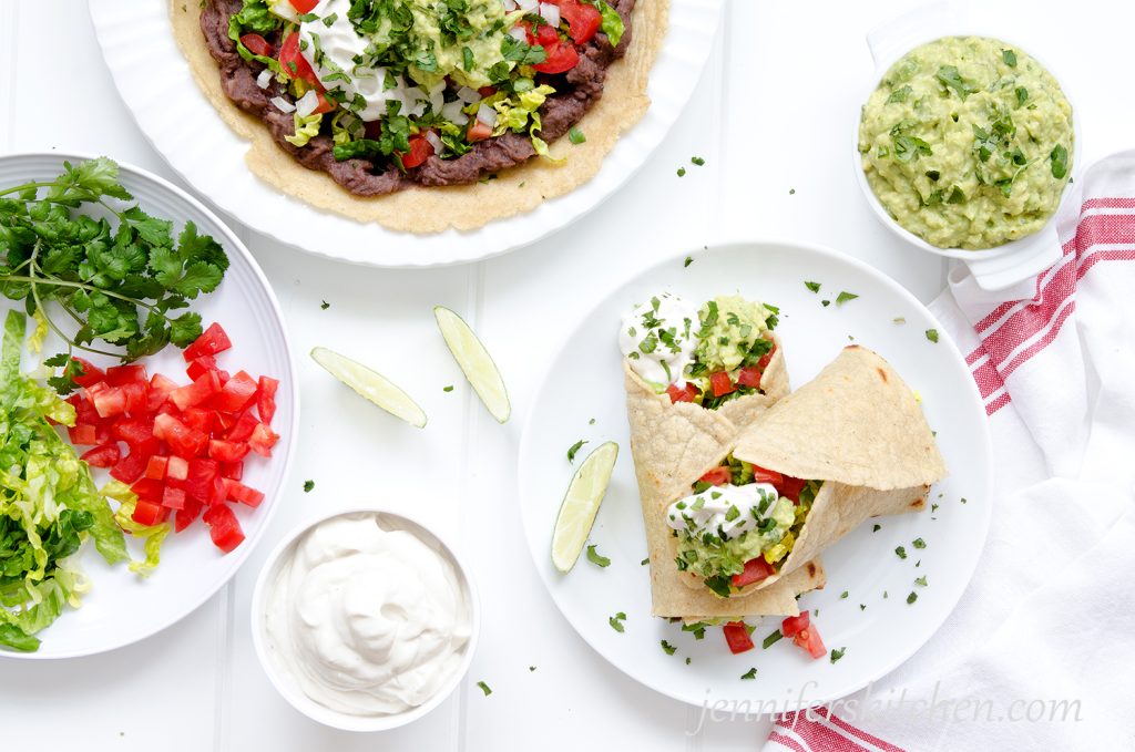 Bean burritos on a plate topped with non-dairy sour cream and guacamole.