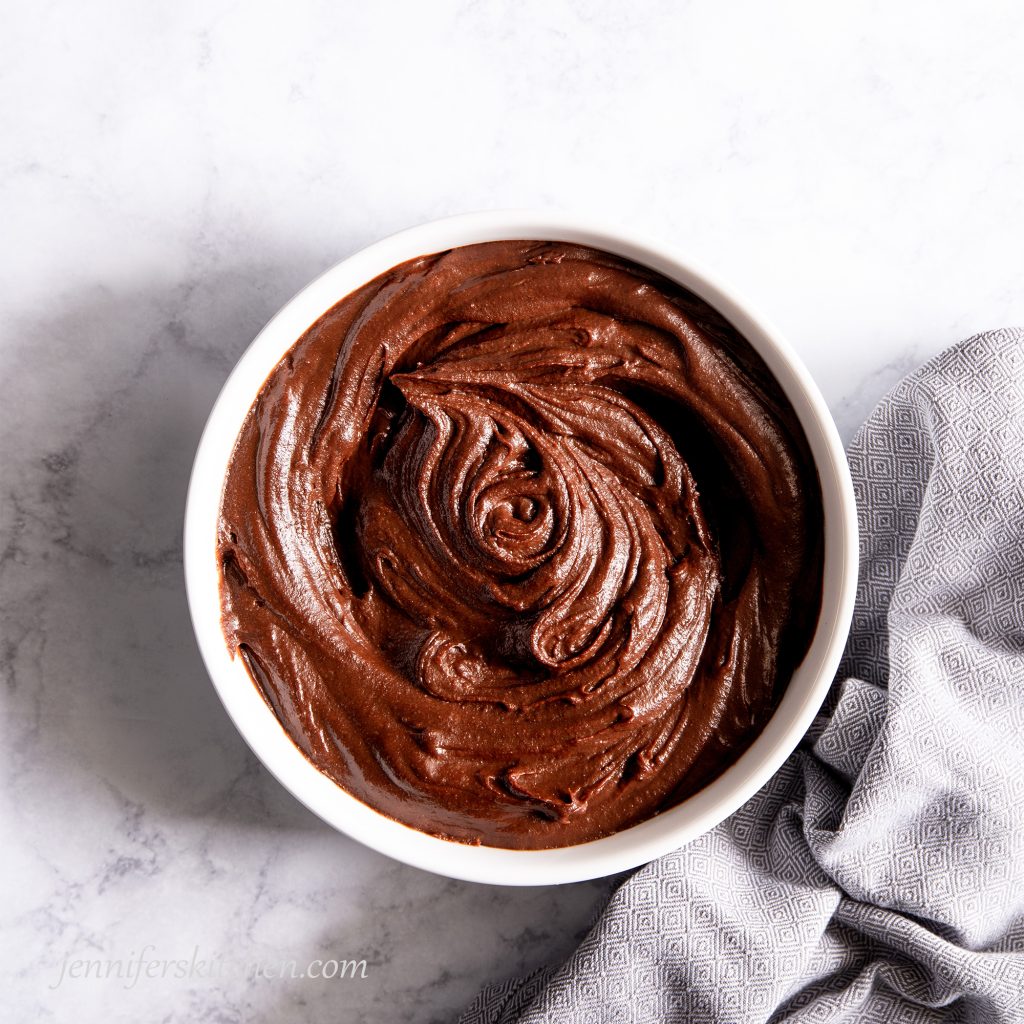 Luscious sugar-free carob frosting swirled in a white bowl with a towel on the side.