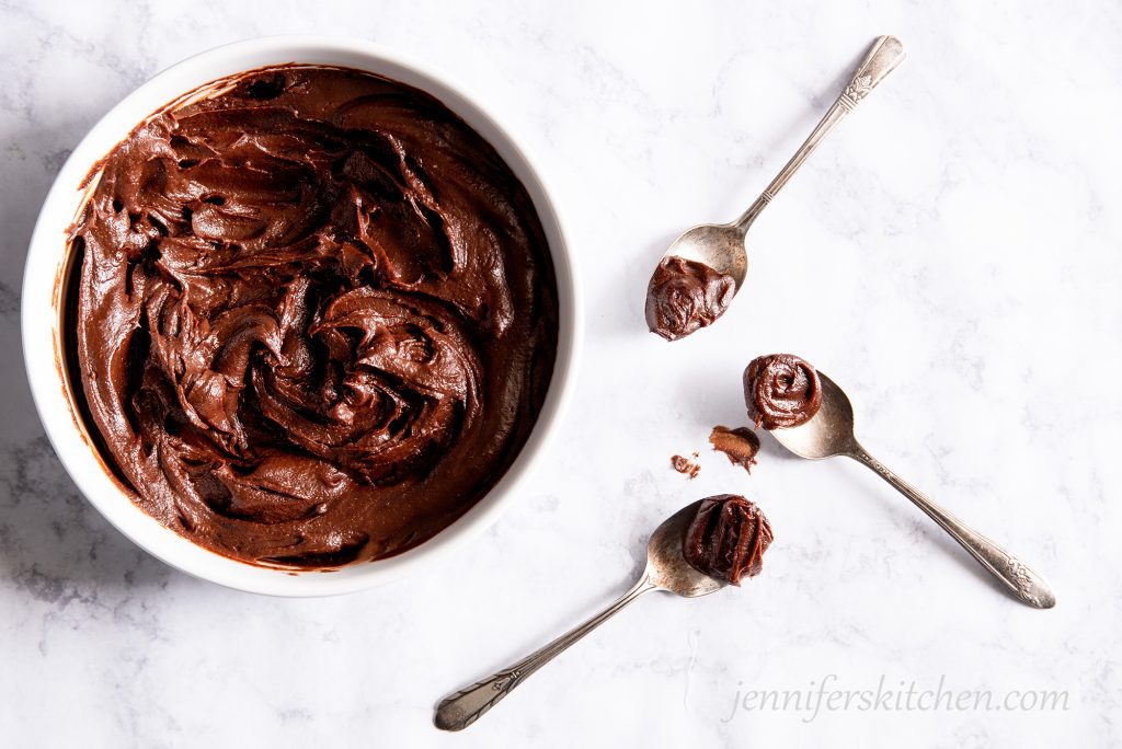 Luscious sugar-free carob frosting in a white bowl with three spoons.