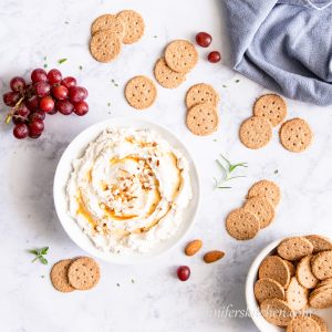 A bowl of vegan almond cheese with crackers and grapes.