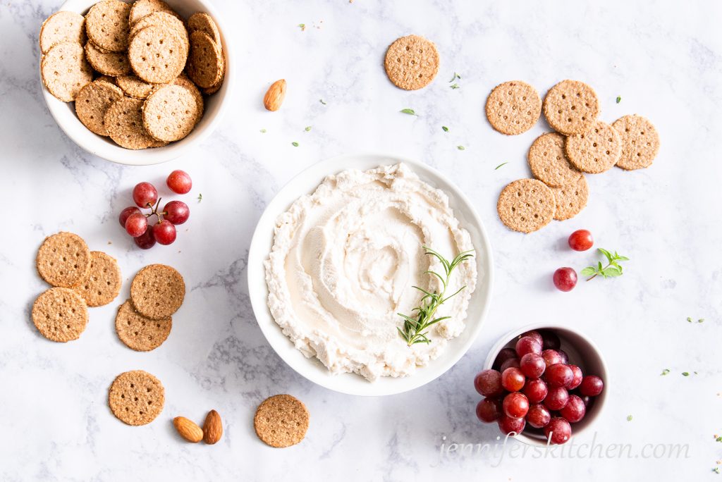 A bowl of vegan almond cheese with crackers and grapes.