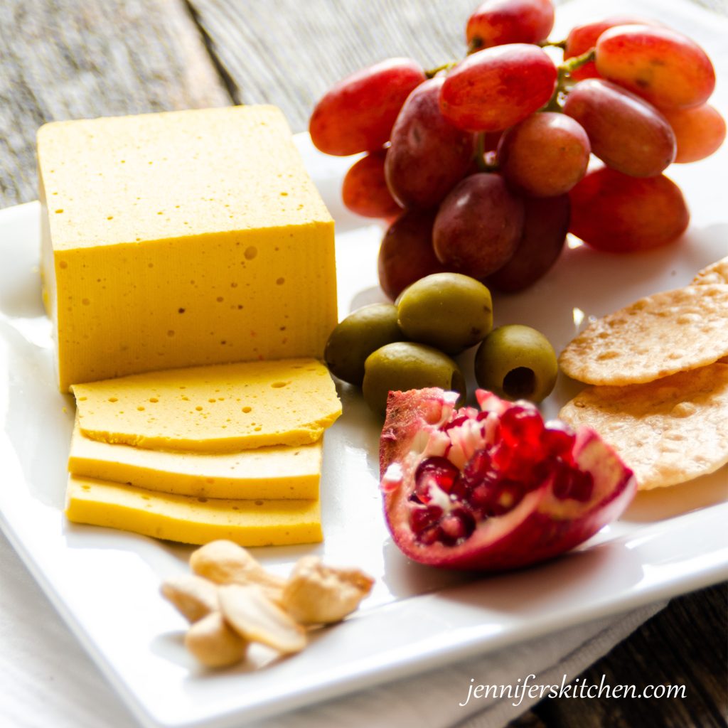 Sliceable vegan cheese with crackers, olives, and fruit on a serving dish