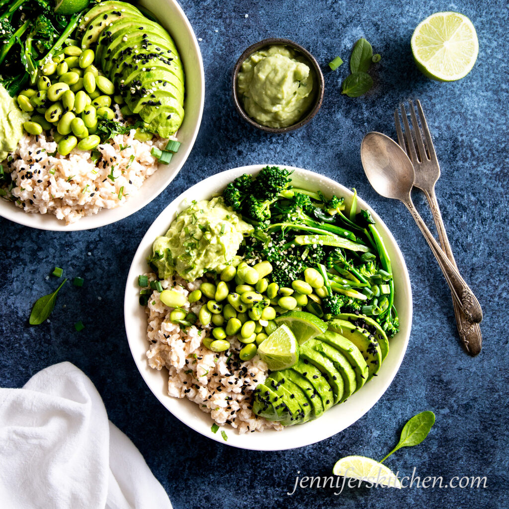 Two Coconut Rice Veggie Bowls with avocado sauce and limes