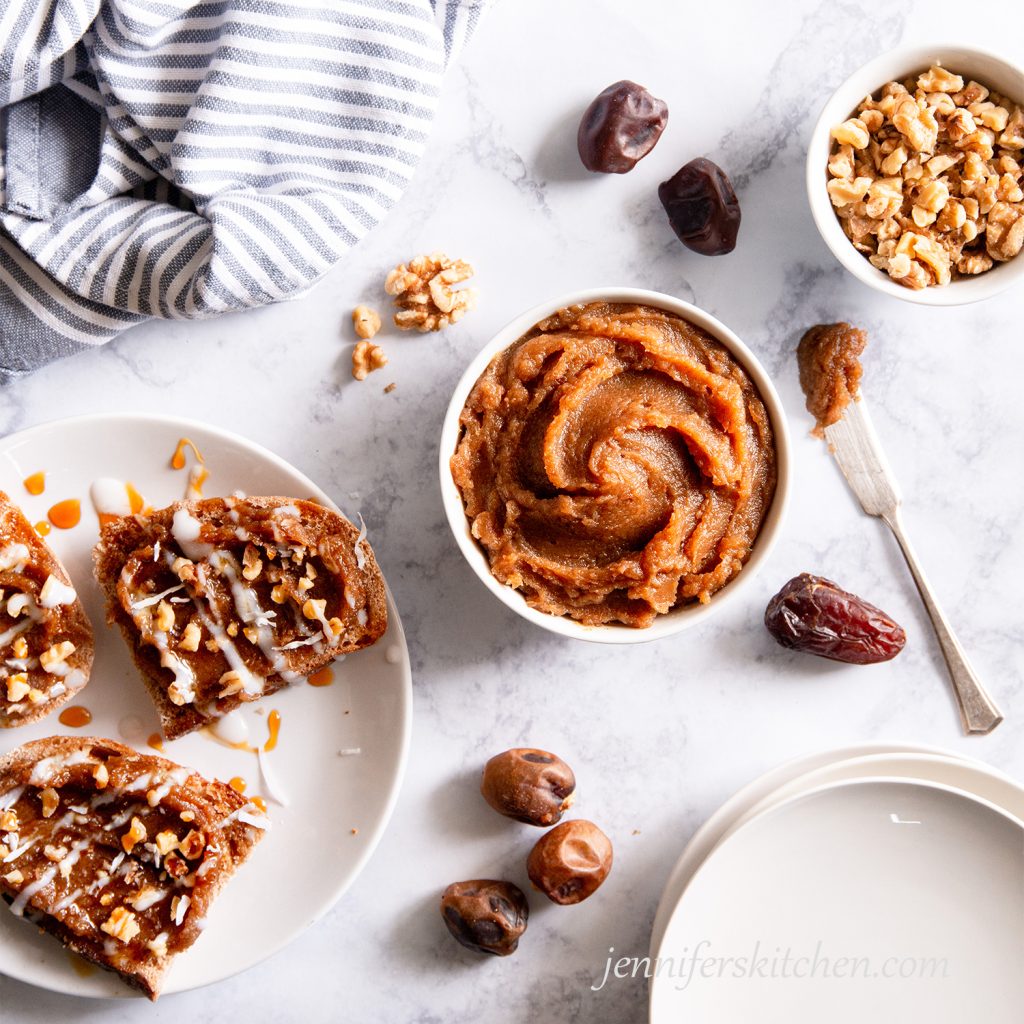 A bowl of date paste with a knife and toast spread with date paste and topped with walnuts.