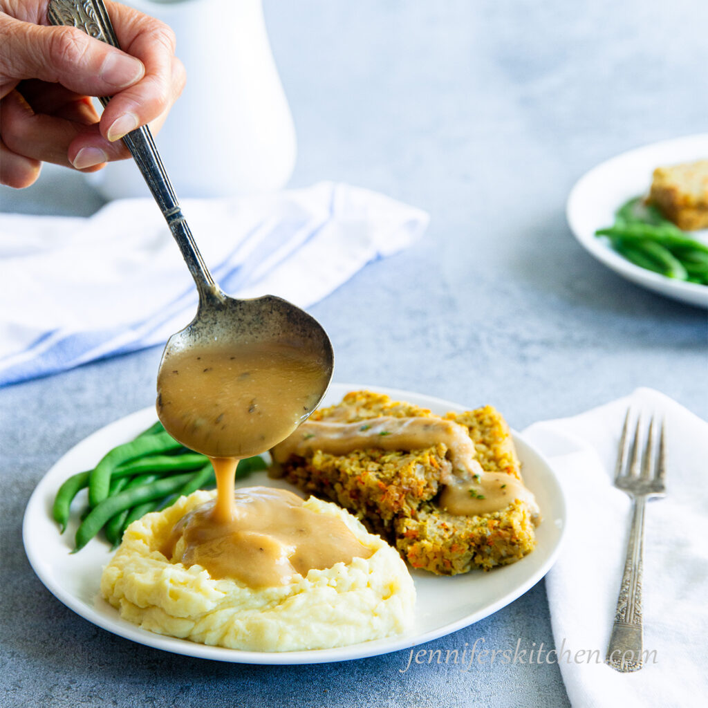 Ladling Chickpea Gravy over mashed potatoes with veggie loaf and green beans on the side.