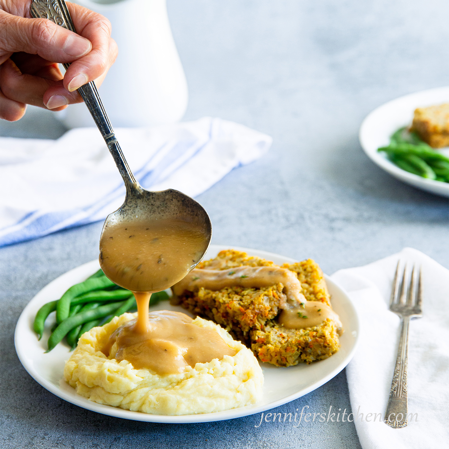 Ladling Chickpea Gravy over mashed potatoes with veggie loaf and green beans on the side.