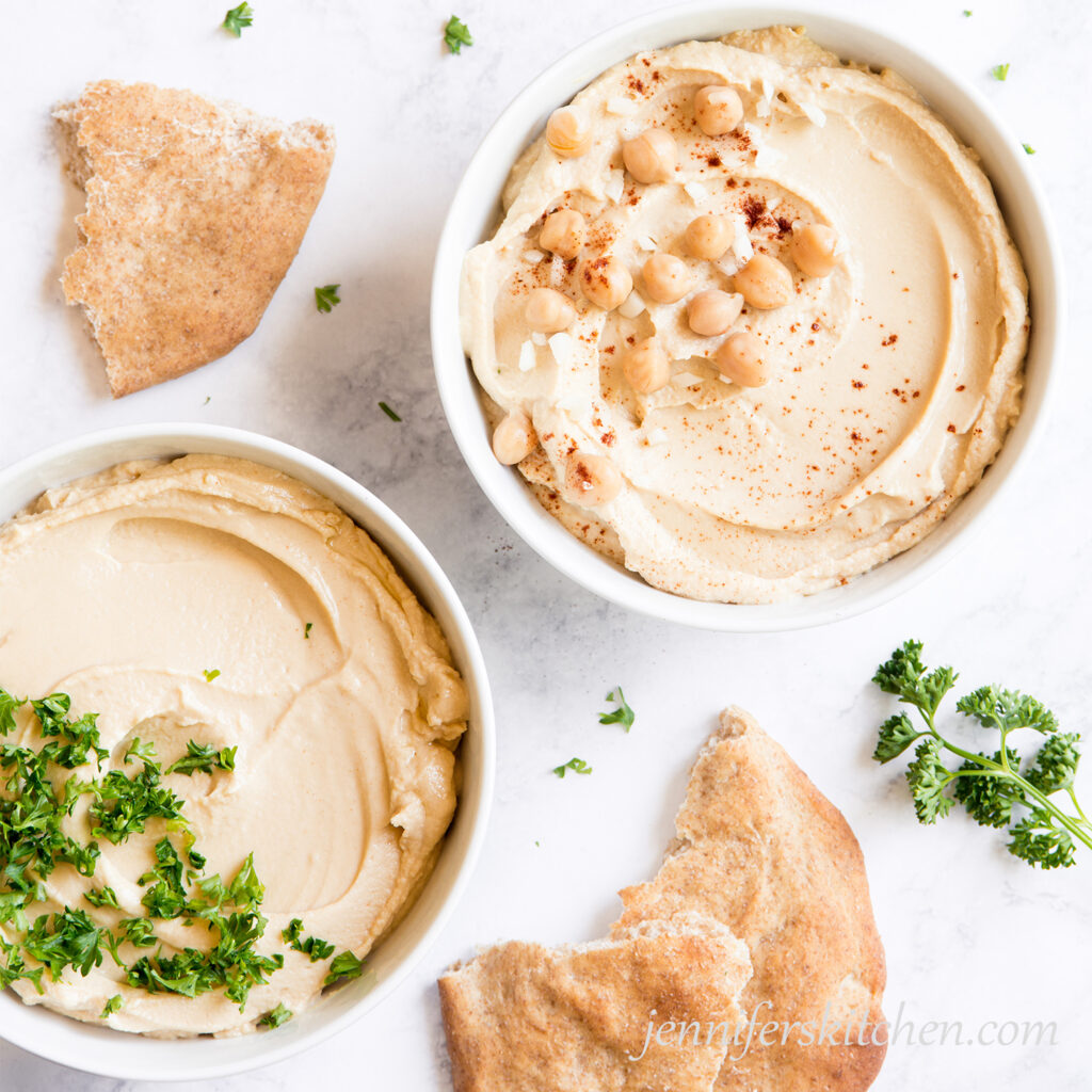 Bowls of oil-free hummus topped with fresh parsley, garlic, and chickpeas with pita bread.