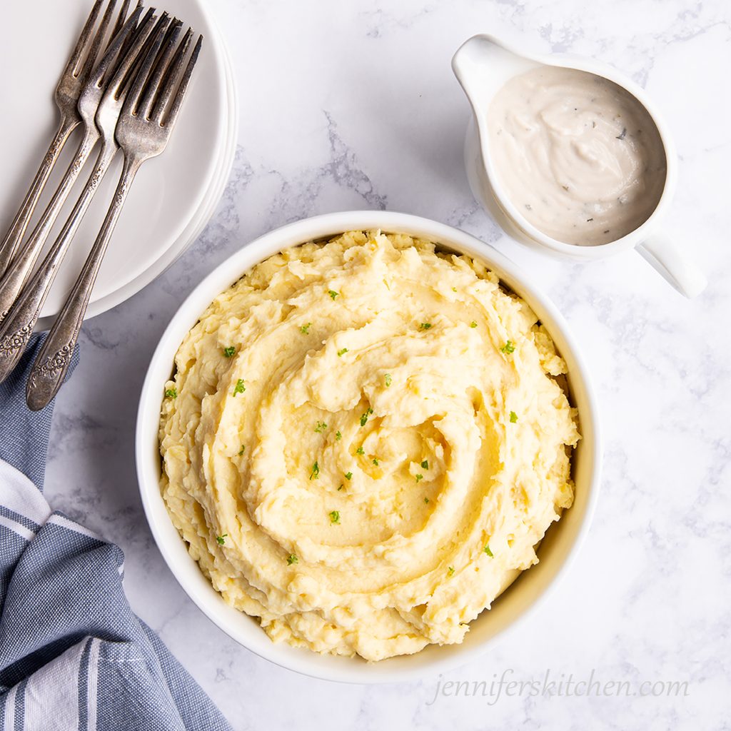 Vegan mashed potatoes in a serving bowl with vegan herb gravy on the side