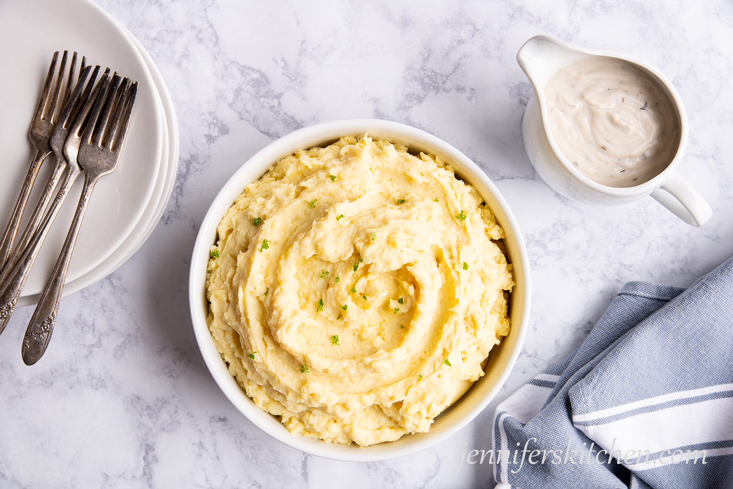 Vegan mashed potatoes in a bowl with gravy on the side and a stack on plates with forks.