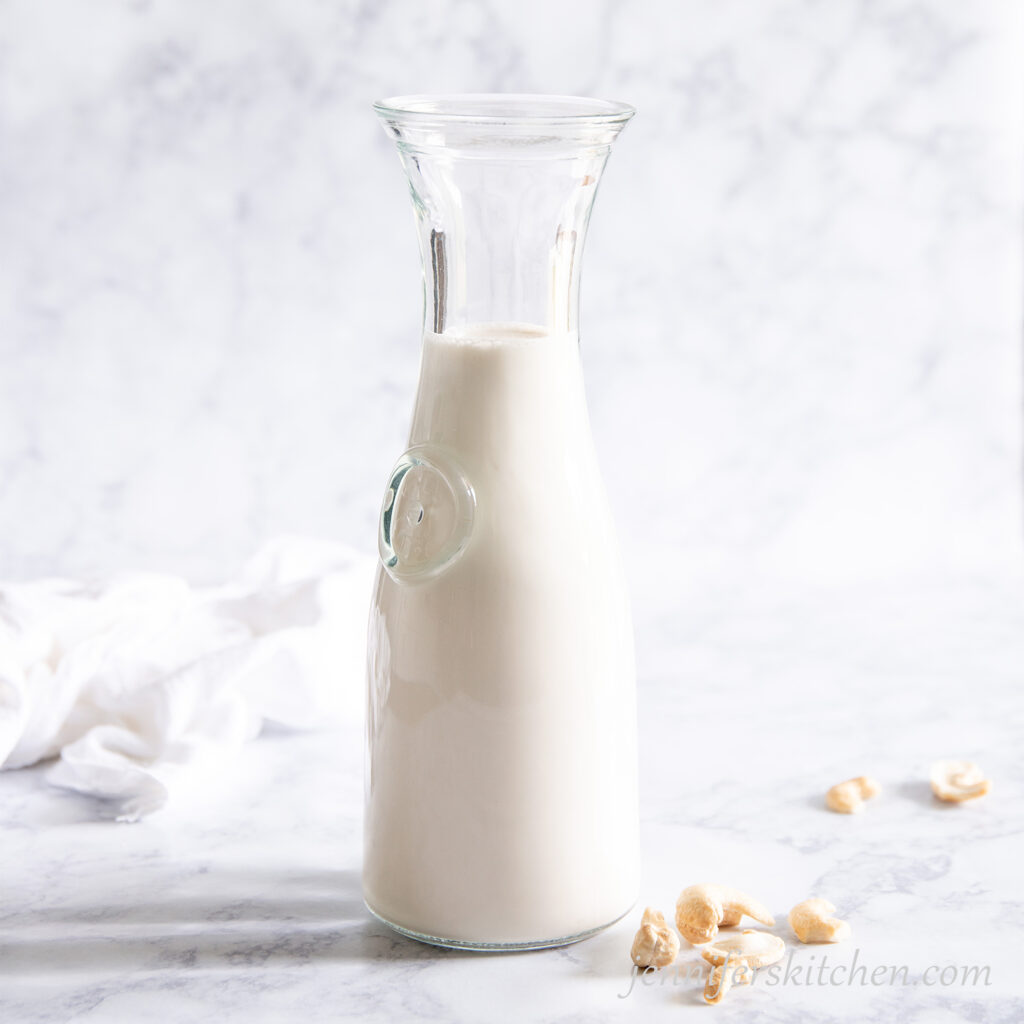 Cashew milk in a milk pitcher with cashews scattered beside.