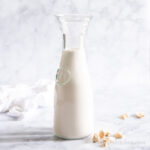 Cashew milk in a milk pitcher with cashews scattered beside.