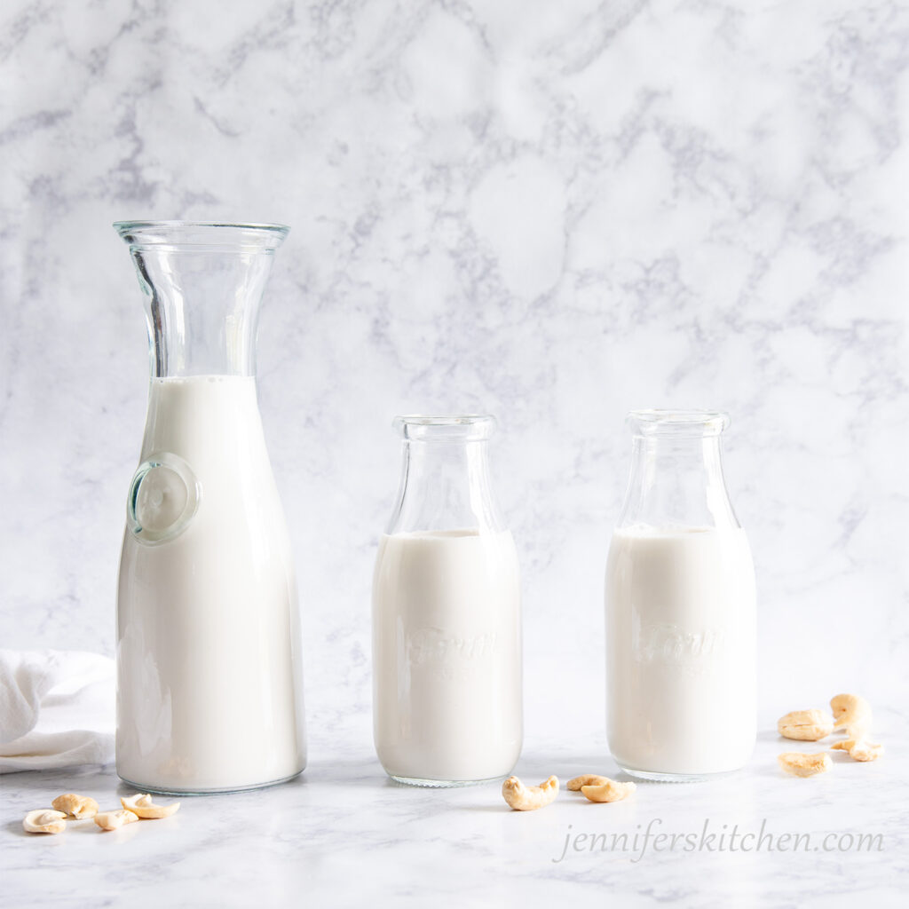 Homemade cashew milk in three milk jars with cashews scattered.