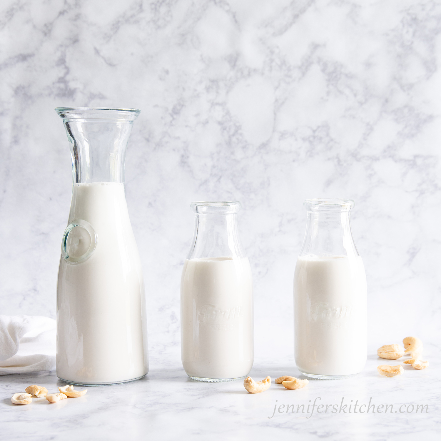 Homemade cashew milk in three milk jars with cashews scattered.