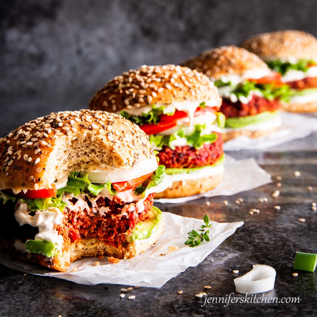 Oil-free beet burgers on a buns with toppings and a delicious bite taken out of one.