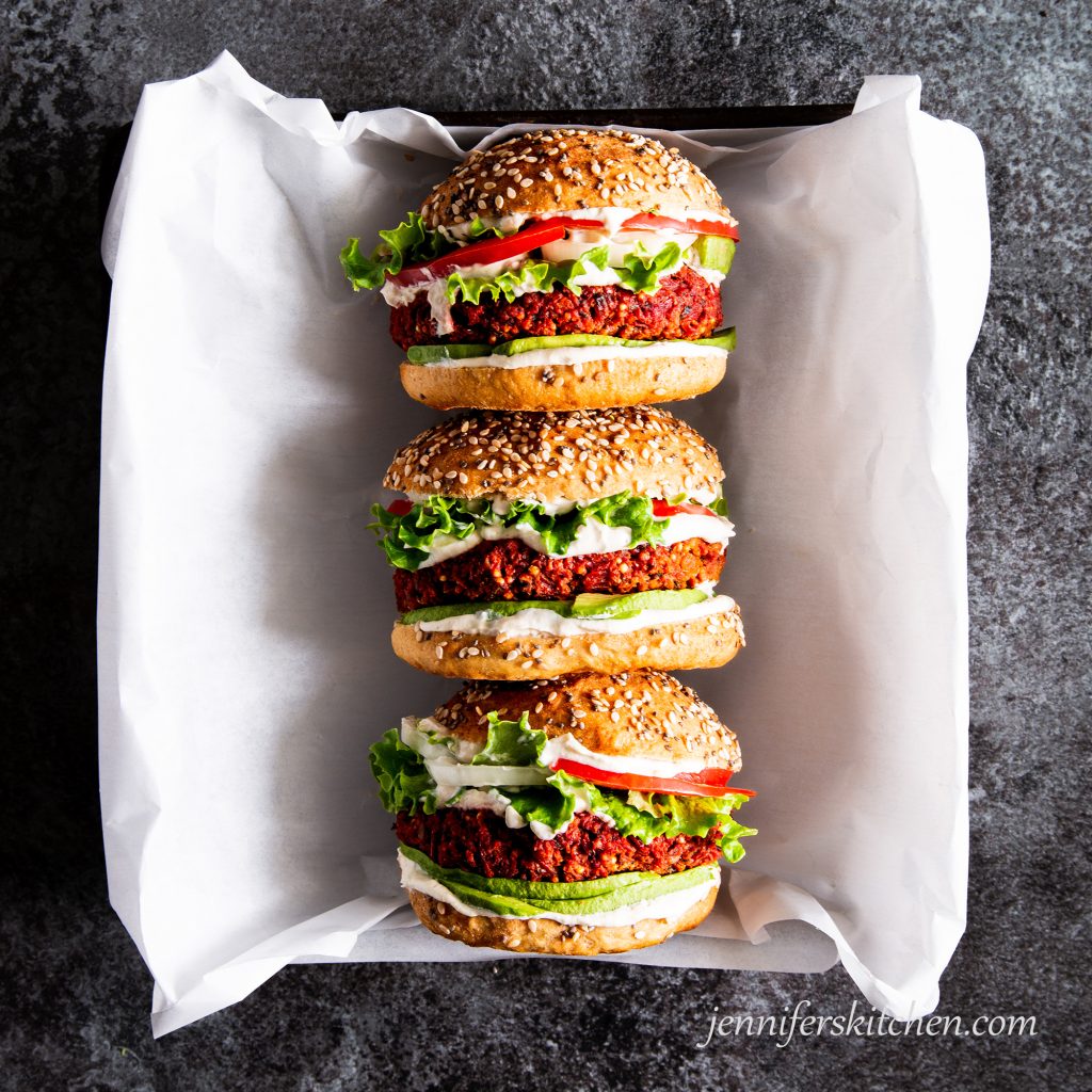 Gluten-free, oil-free beet burgers on a buns with toppings in serving dish.