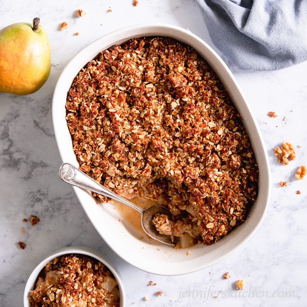 Sugar-Free, Oil-Free, Gluten-Free Pear Crisp in a white casserole dish with a spoon and a bowl on the side.