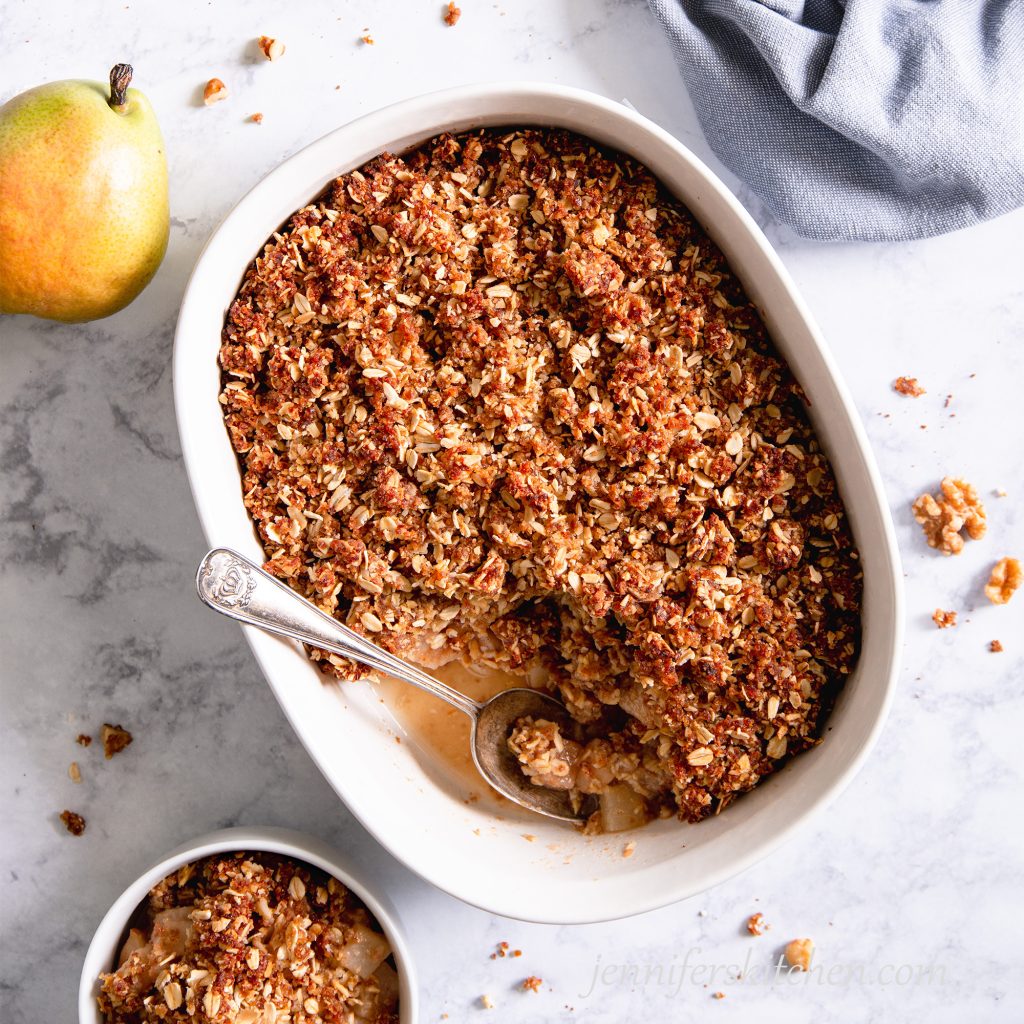 Sugar-Free, Oil-Free, Gluten-Free Pear Crisp in a white casserole dish with a spoon and a bowl on the side.