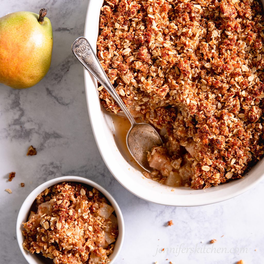 Sugar-Free, Oil-Free, Gluten-Free Pear Crisp in a white casserole dish with a spoon and bowl on the side.