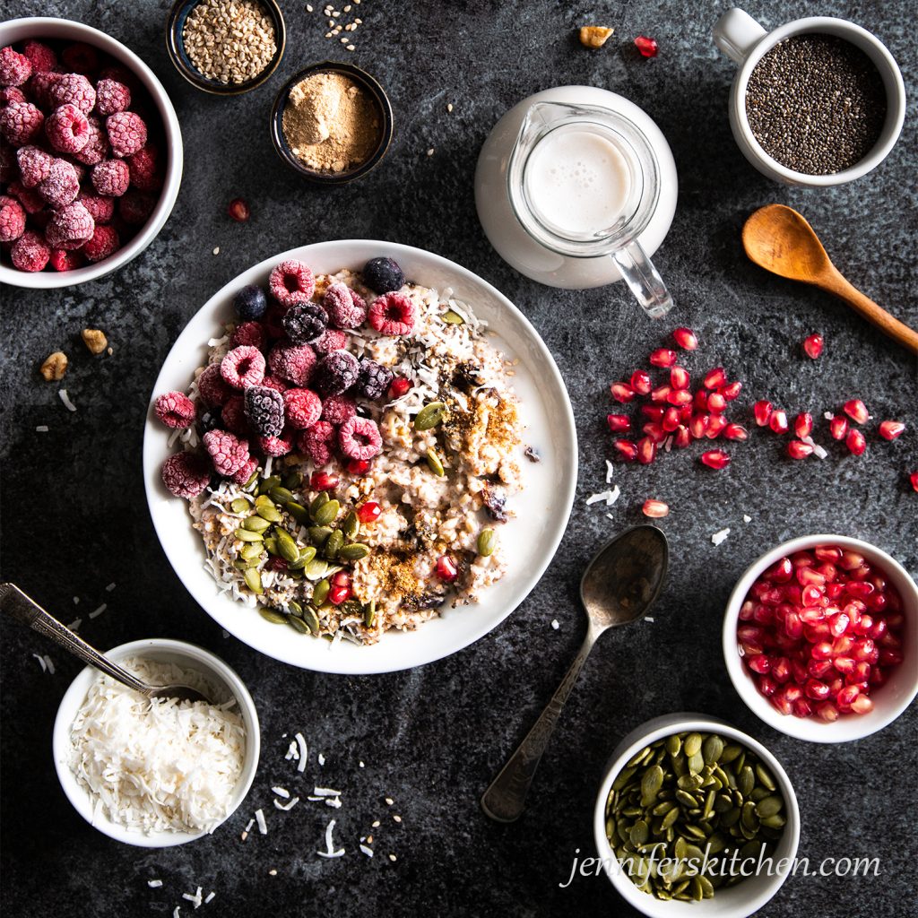 A breakfast of Power Porridge with raspberries, pumpkin seeds, coconut, chia seeds, sesame seeds, date sugar, coconut milk, and pomegranate seeds.