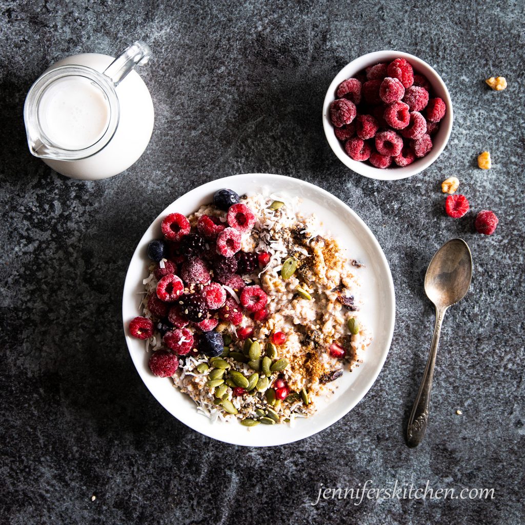 A bowl of Power Porridge topped with raspberries, pumpkin seeds, coconut, chia seeds, sesame seeds, date sugar, coconut milk, and pomegranate seeds.