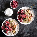 Two bowls of Power Porridge topped with raspberries, pumpkin seeds, coconut, chia seeds, sesame seeds, date sugar, coconut milk, and pomegranate seeds.