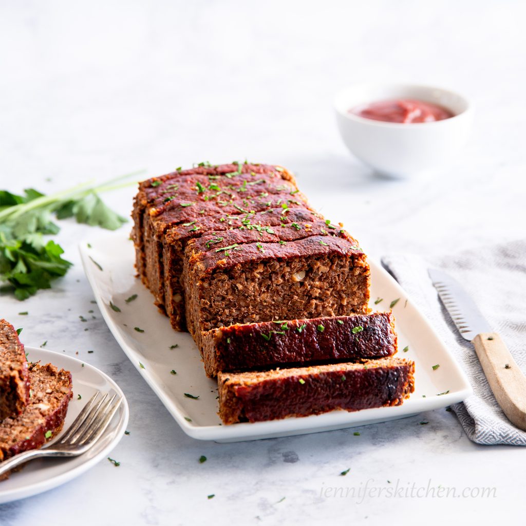 Gluten-free Quinoa Lentil No-Meatloaf on a platter with a plate of meatloaf on the side.