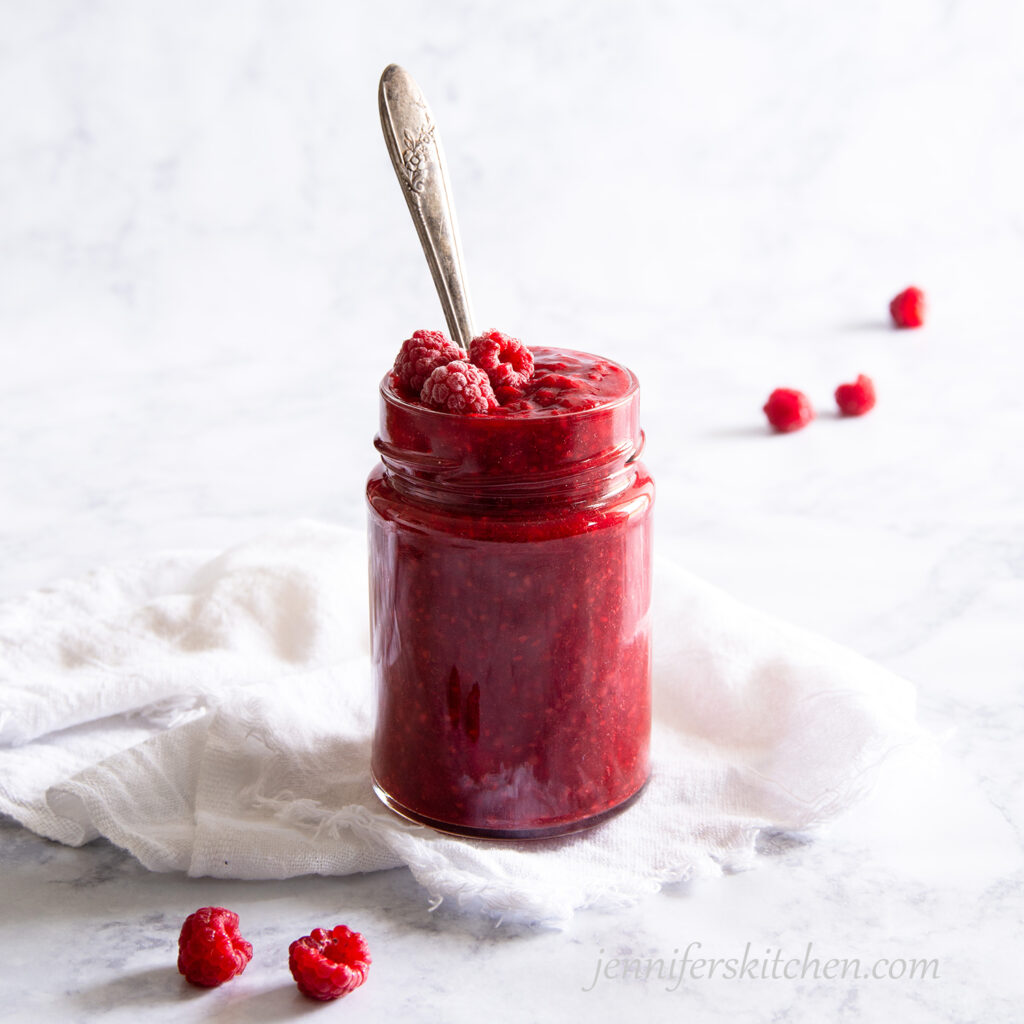 A jar of Sugar-Free Raspberry Jam topped with raspberries.