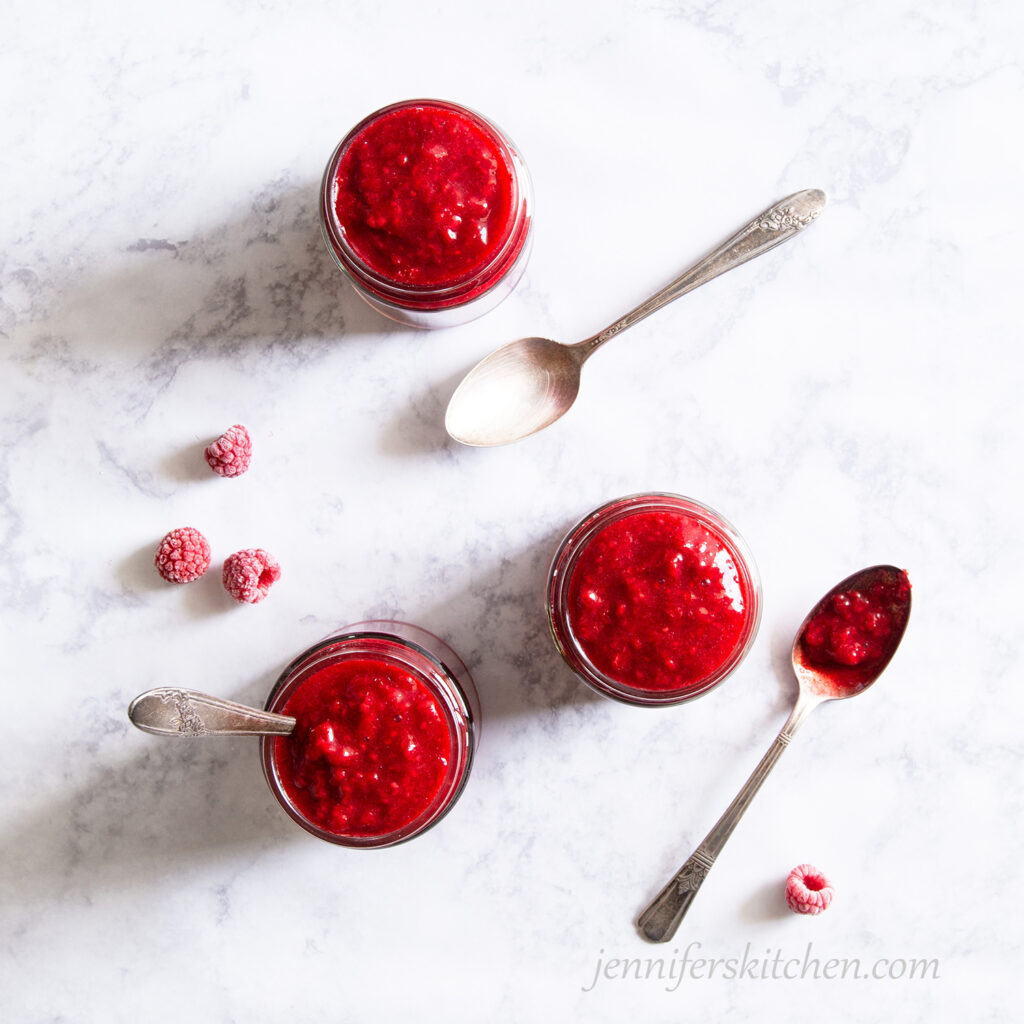 Three jars of Sugar-Free Raspberry Jam with serving spoons and raspberries.