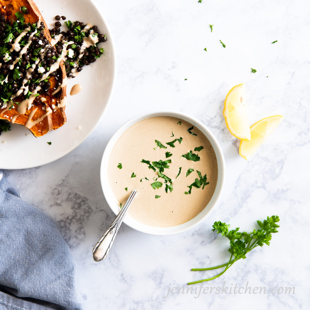 Tangy Tahini Sauce in a bowl with lentils and sweet potatoes on the side.