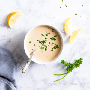 Tangy Tahini Sauce in a bowl with fresh parsley and lemons on the side.