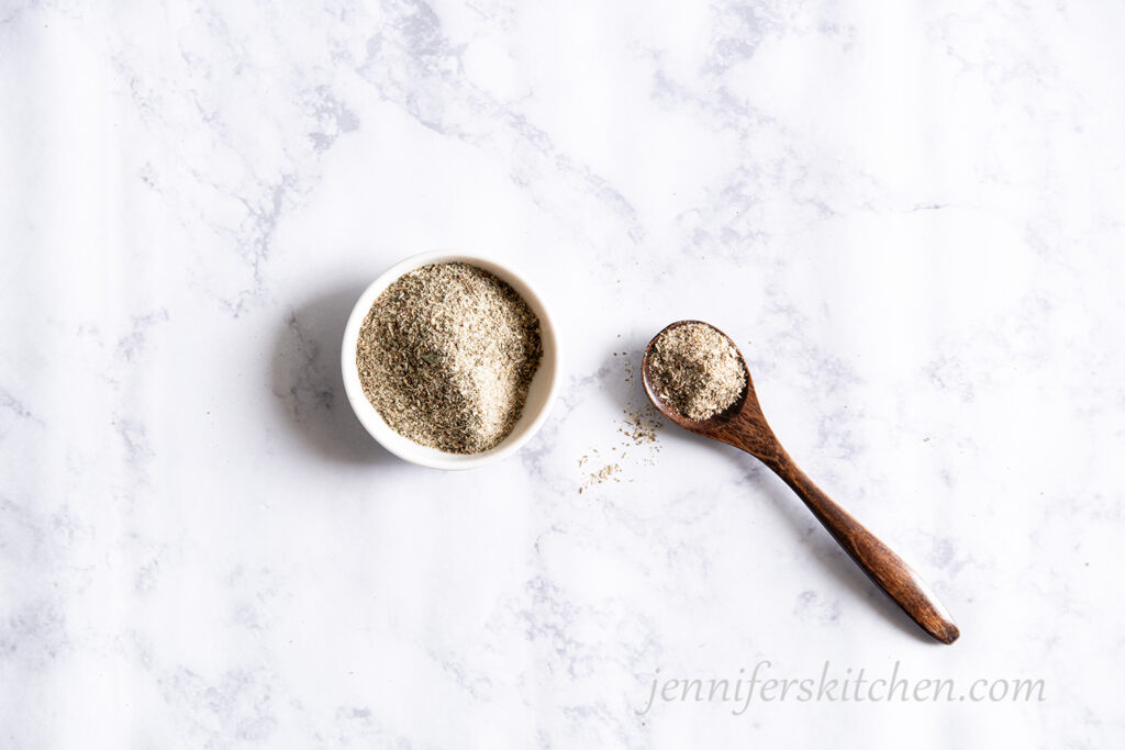 Nutritional yeast free vegan chicken seasoning in a little white bowl with a wooden spoon.