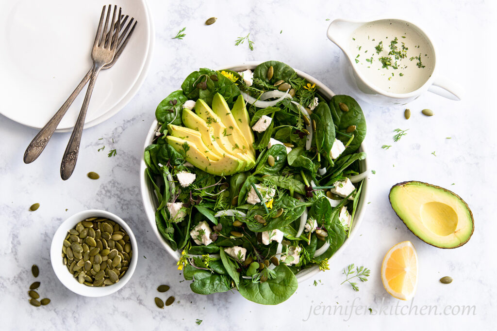 Spinach Avocado Salad with serving plates and Pumpkin Seed Dressing