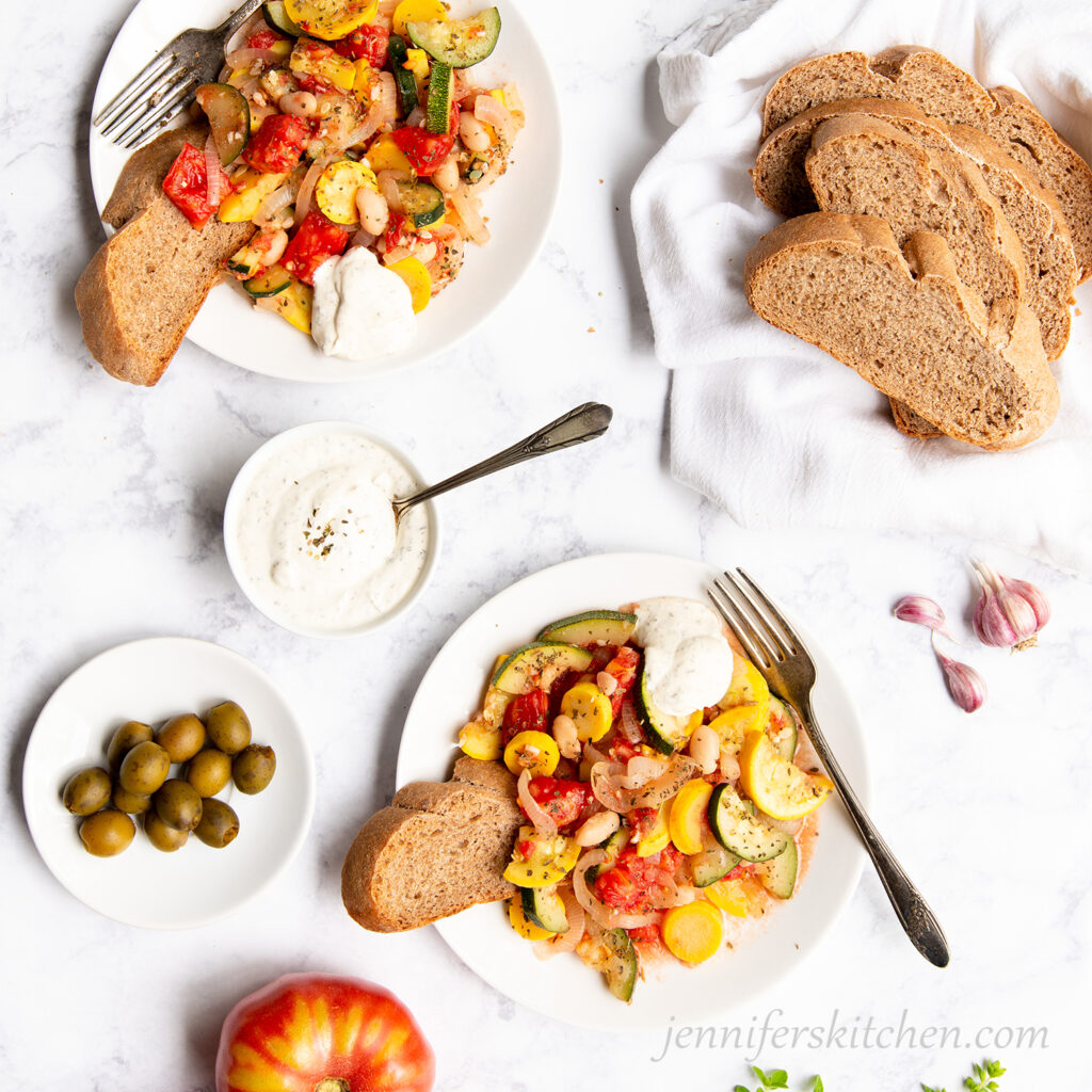Summer Squash Sauté served on 2 white plates with bread and cashew dressing.