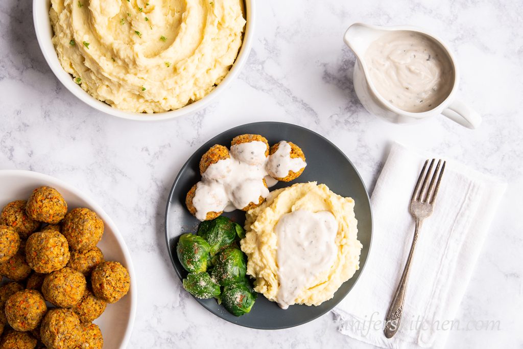 Mashed potatoes with gravy, vegan veggie balls, and brussel sprouts on a plate with a fork on the side.